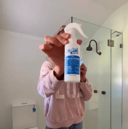 Customer holding EnduroShield bottle in front of clean shower