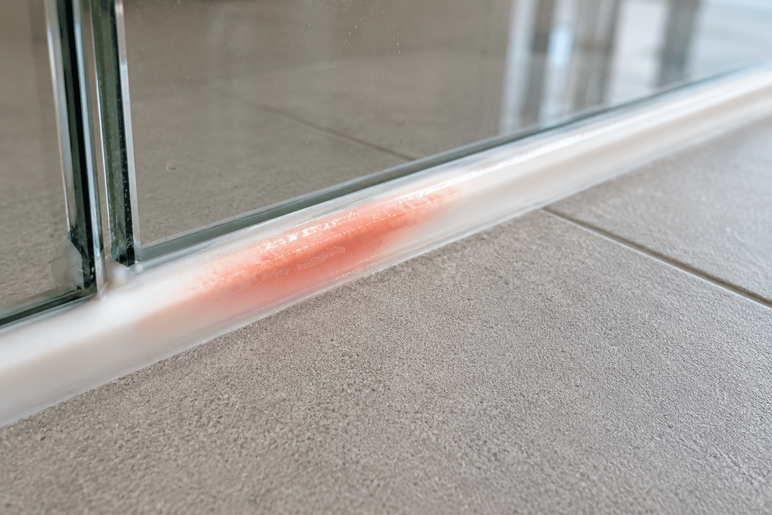 Pink Serratia marcescens bacterial film on white silicone caulk in Malaysian shower