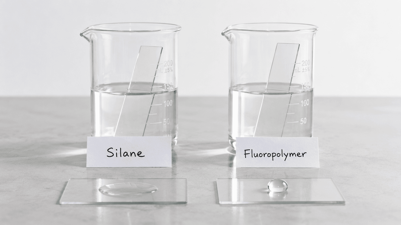 Two glass coating sample panels on a bathroom workbench showing haze versus clear water beading