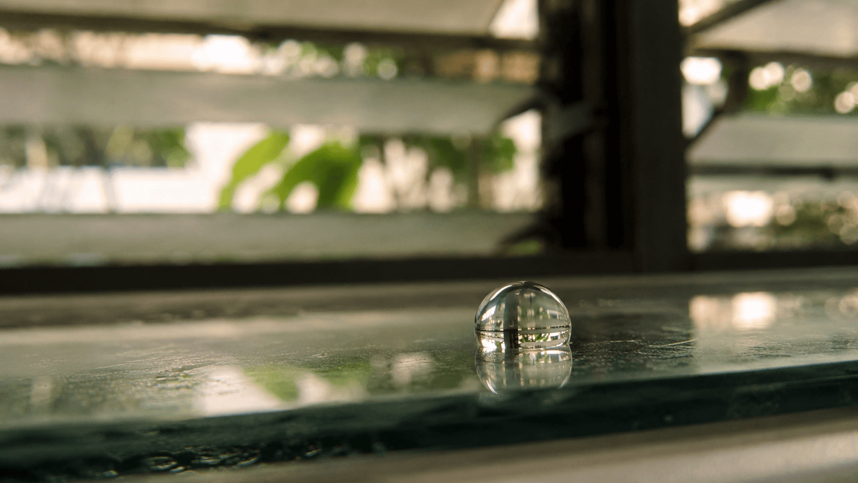Macro shot of a perfect water droplet at 110-degree contact angle on glass — the geometric signature of a hydrophobic coating